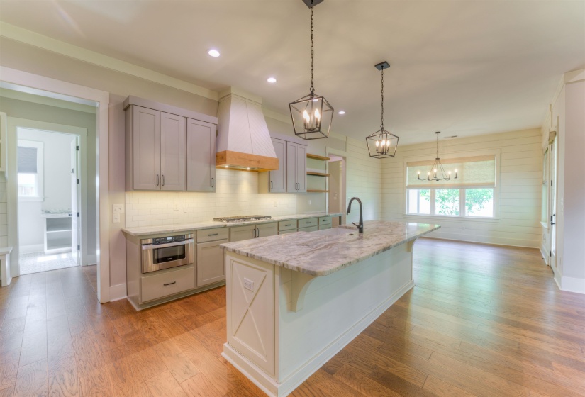 Modern kitchen featuring a large island with a stone countertop, gray cabinetry, white subway tile backsplash, and wood-finish flooring