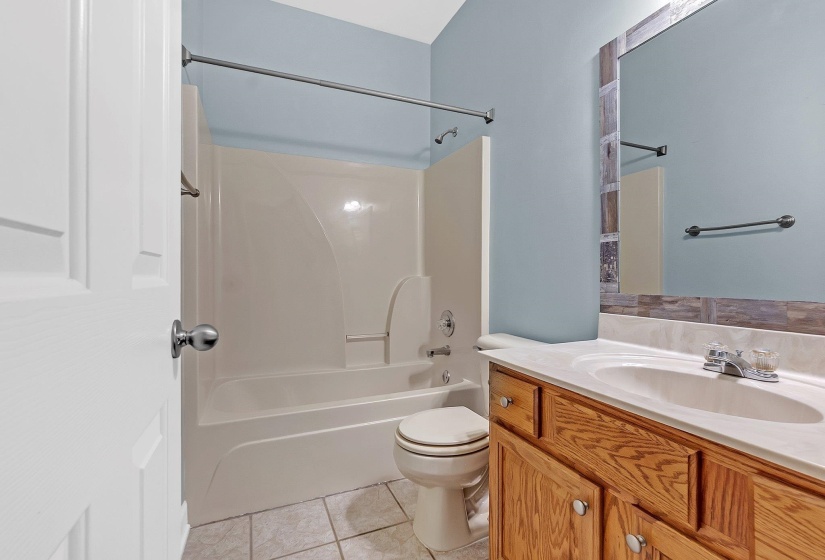 Bathroom featuring a vanity with a white countertop and integrated sink, wood-finish cabinetry, and a mirror with a decorative frame