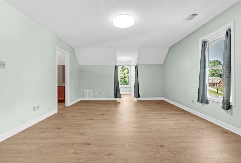 Spacious bedroom featuring light wood-finish flooring, light green wall paint, white trim, and white ceilings. Bathroom attached.