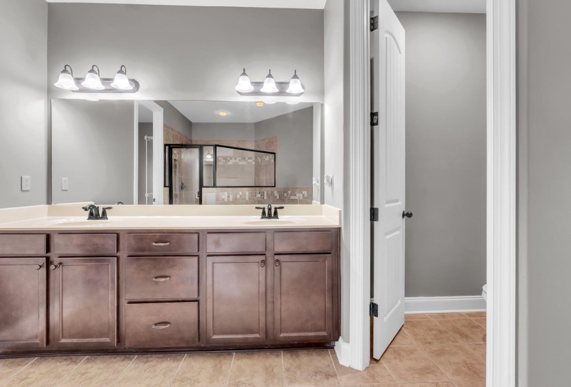 Bathroom featuring a dual vanity with a light-toned countertop, brown cabinetry, and two sets of overhead wall sconces