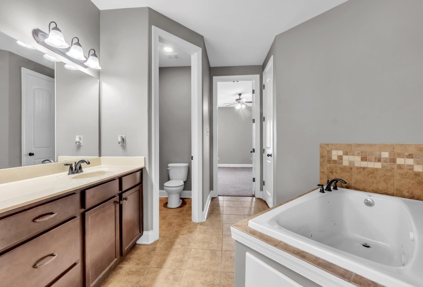 Bathroom featuring a built-in soaking tub with tile surround, a dual-sink vanity with a light-toned countertop, and warm-toned floor tiles