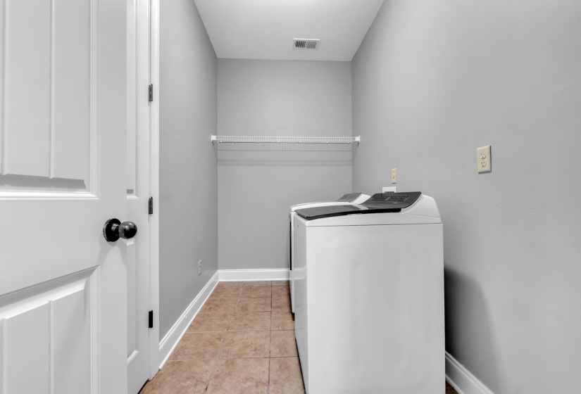 Utility area featuring tile flooring, neutral wall tones, white baseboards, and a wire shelving unit. Pantry is located in the laundry room.