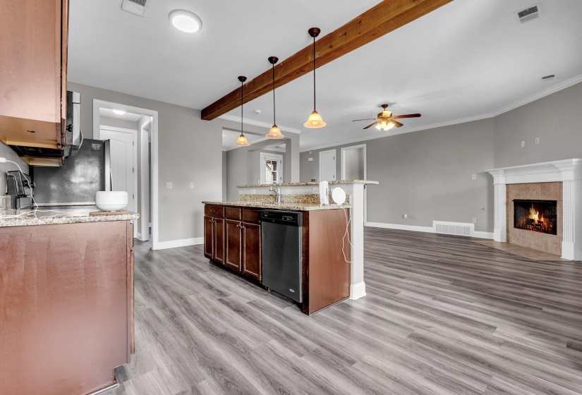 Open-concept living space featuring wood-finish flooring, a kitchen island with stone countertops, dark wood cabinetry, a built-in dishwasher, and pendant lighting