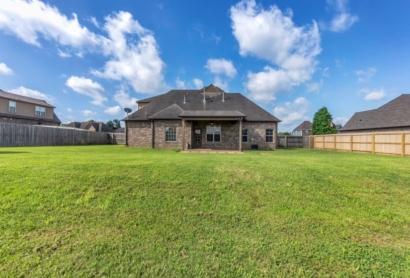 Expansive green lawn bordering a brick exterior residence with a covered patio