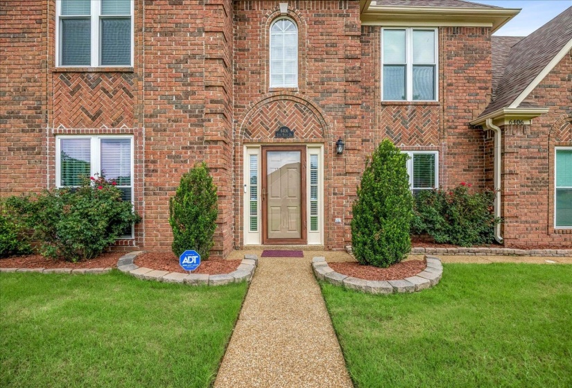 Brick facade residence featuring a peaked roofline, decorative arched entryway, and a ground-level planter with stone edging