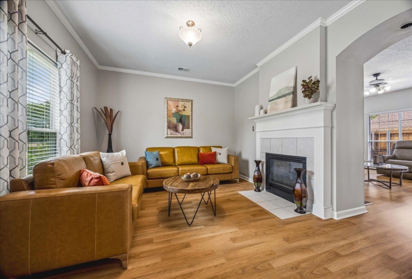 Spacious living area featuring wood-finish flooring, a white mantel fireplace with tile surround, an arched entryway, crown molding, and recessed lighting