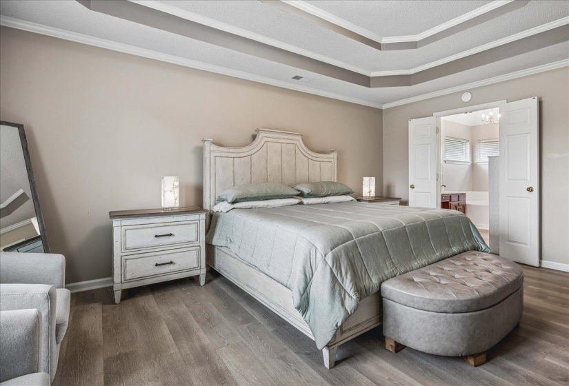 Recessed tray ceiling with crown molding, wood-finish flooring, and neutral wall tones