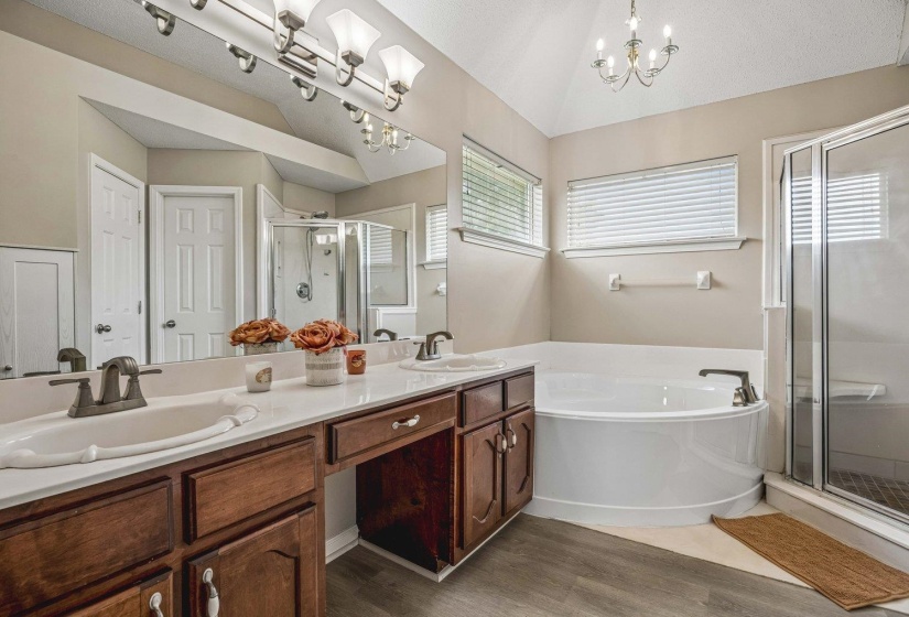 Bathroom featuring a double vanity with white countertops, warm wood cabinetry, an oval soaking tub, a separate glass-enclosed shower, and wood-finish flooring