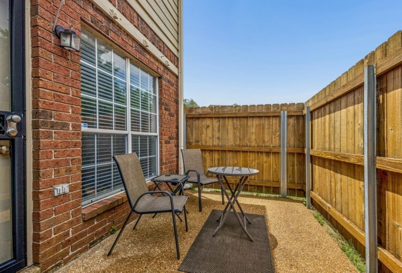 Private outdoor patio featuring a gravel surface, wood privacy fencing, and brick exterior with a large window