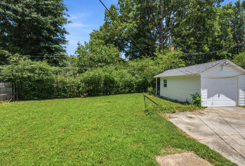 Expansive grassy yard with mature perimeter foliage, a wooden fence, and a detached two-car garage featuring a white overhead door and a side entry
