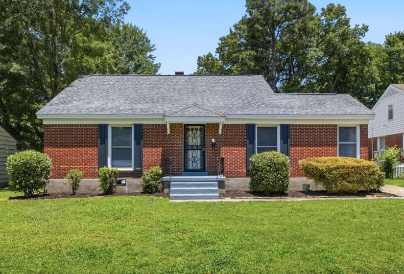 Brick facade residence featuring a front yard with mature landscaping, a dark gray shingle roof, and a privacy screen door