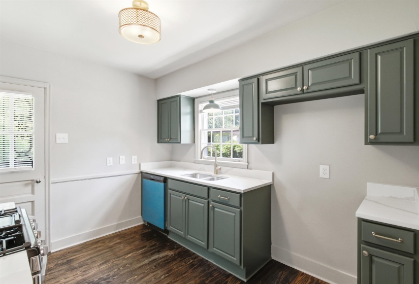 Kitchen featuring dark green cabinetry, white countertops, a double basin sink, wood-finish flooring, and a door with louvered window
