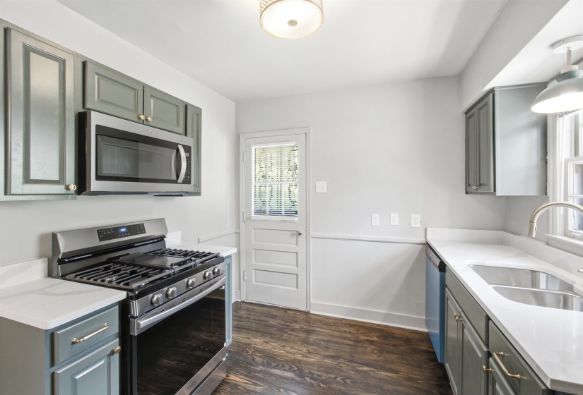 Kitchen featuring wood-finish flooring, stainless steel appliances, light gray cabinetry with gold-tone hardware, white countertops, and a white paneled door with glass inserts