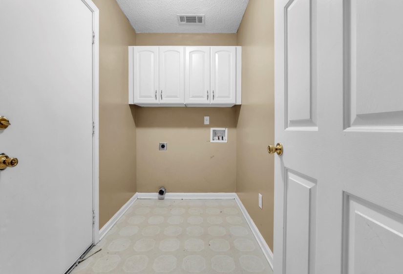 Utility area featuring light beige walls, white cabinetry, and patterned vinyl flooring