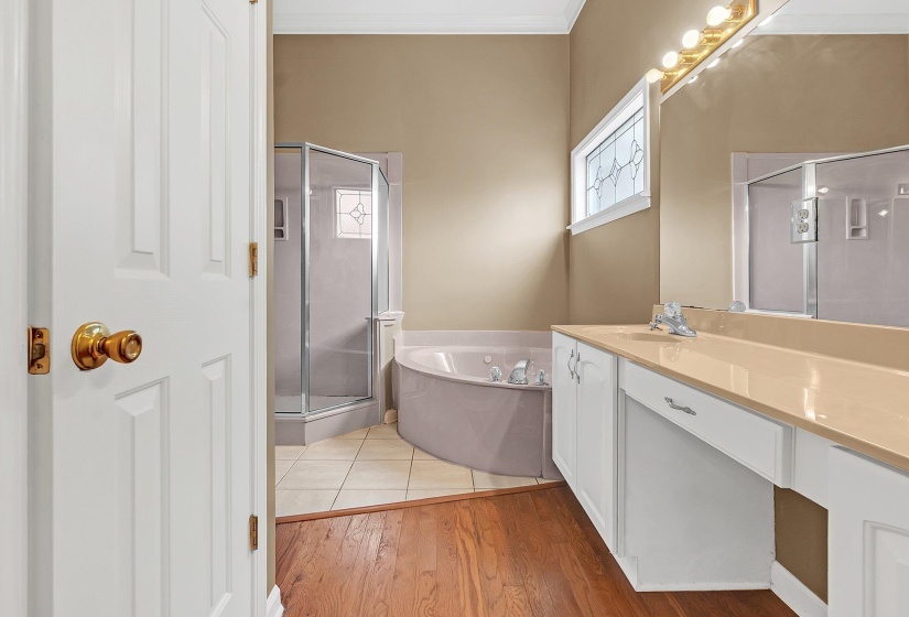Bathroom featuring a large vanity with an integrated sink, white cabinetry, a corner shower, a corner soaking tub, and a decorative frosted window