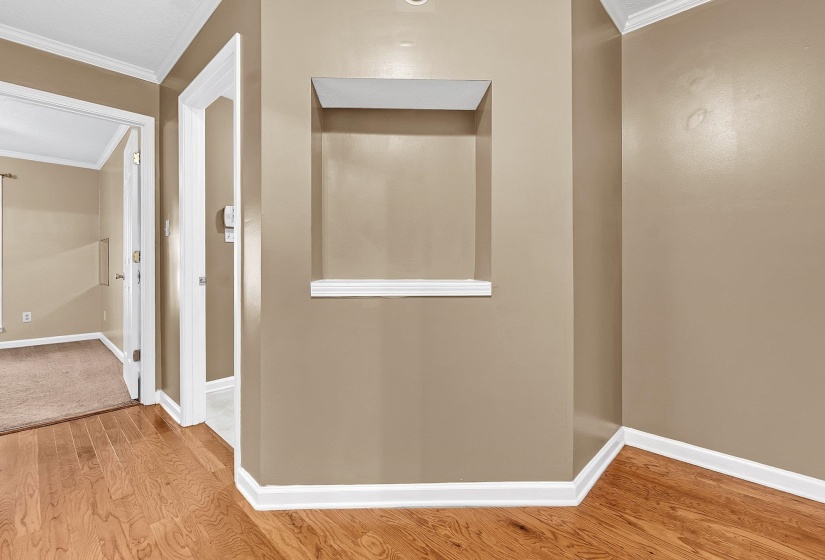 Hallway featuring wood-finish flooring, a recessed wall niche with display shelf, crown molding, and neutral wall tones