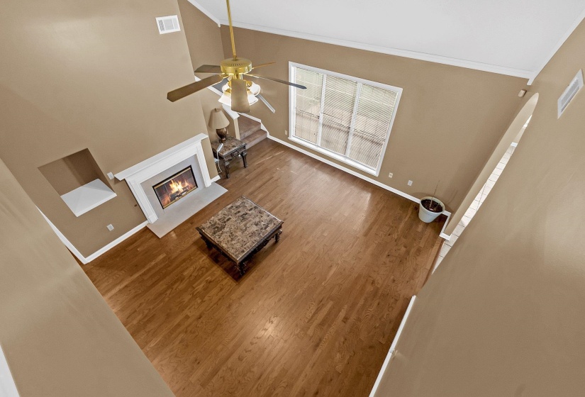 Vaulted ceiling living area featuring wood-finish flooring, a white-mantled fireplace, a ceiling fan fixture, and a multi-pane window