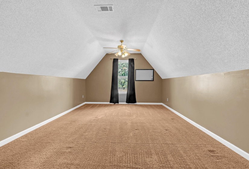 Spacious room featuring vaulted ceilings, neutral-toned carpeting, and a ceiling fan