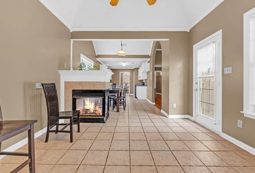 Open concept living area featuring vaulted ceilings, tile flooring, a fireplace with a tiled surround and white mantel, and a glass-paned exterior door
