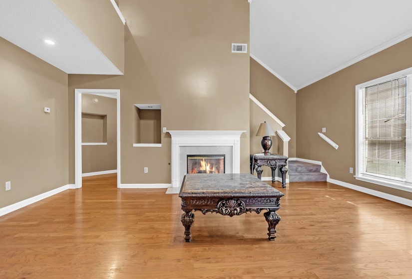 Living area featuring wood-finish flooring, a fireplace with a white mantel, and a multi-level ceiling
